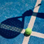 Ombre d'une raquette et balle de tennis sur un court bleu.