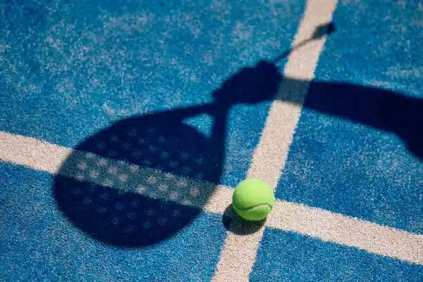 Ombre d'une raquette et balle de tennis sur un court bleu.