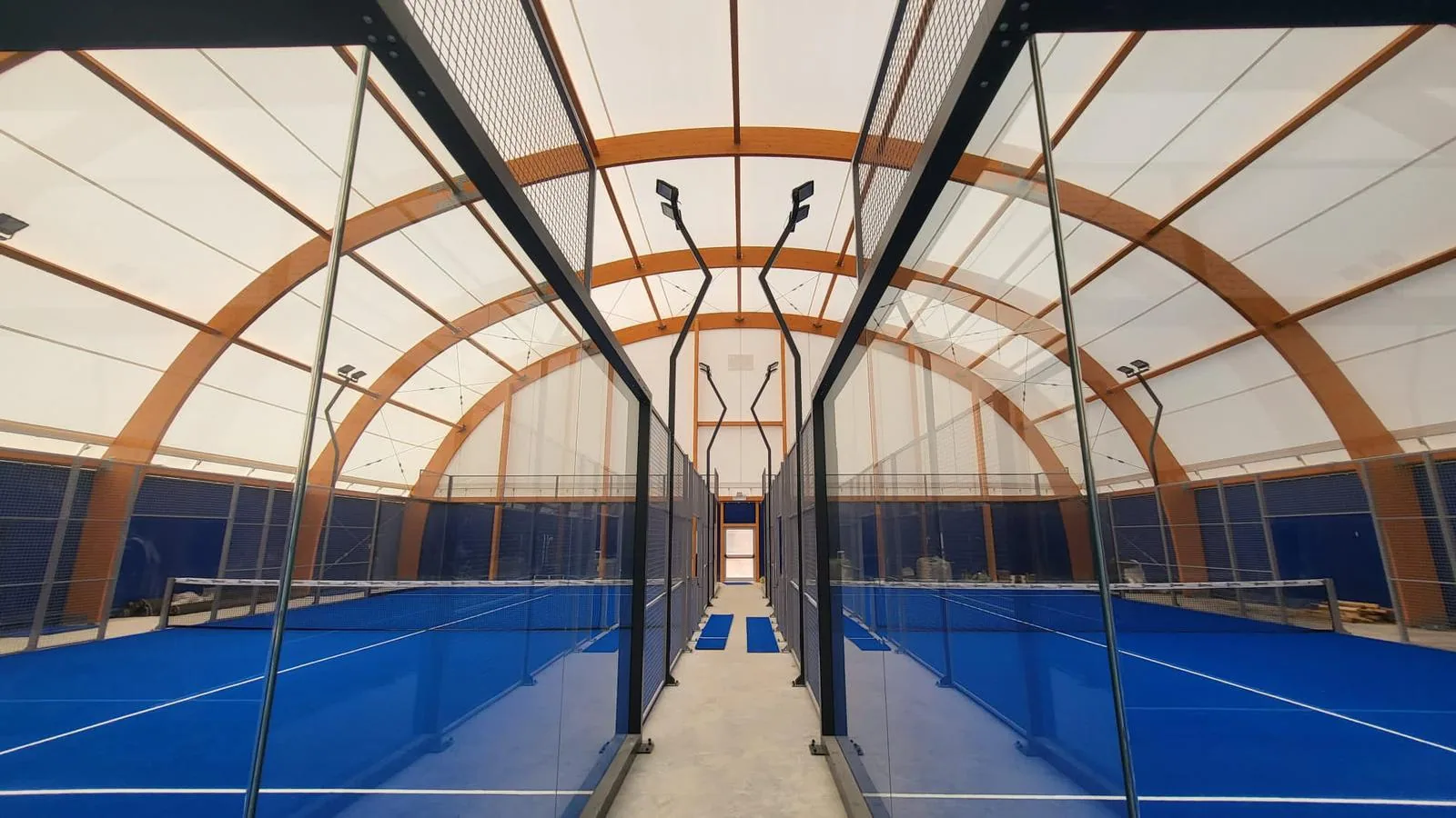 Allée centrale entre terrains de padel sous une couverture en bois