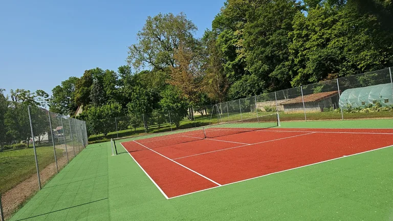 Court de tennis à aire de jeu rouge et abords verts sous un ciel bleu