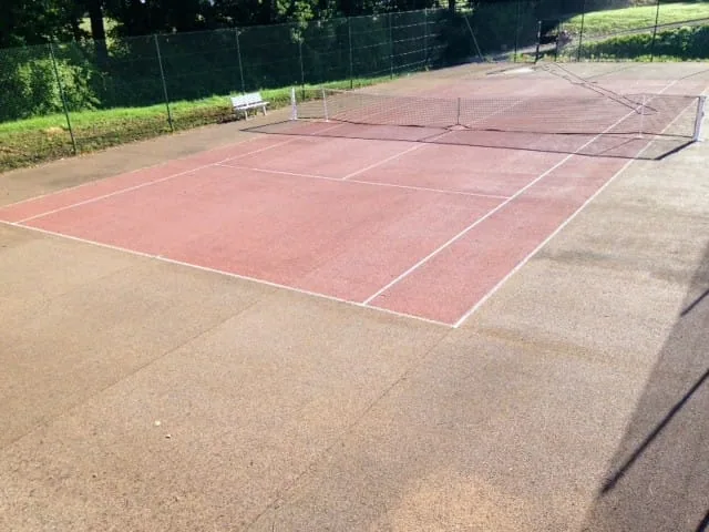 Court de tennis à la peinture rose délavée avant rénovation
