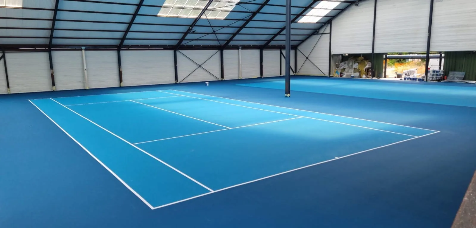 Court de tennis bleu intérieur sous charpente métallique