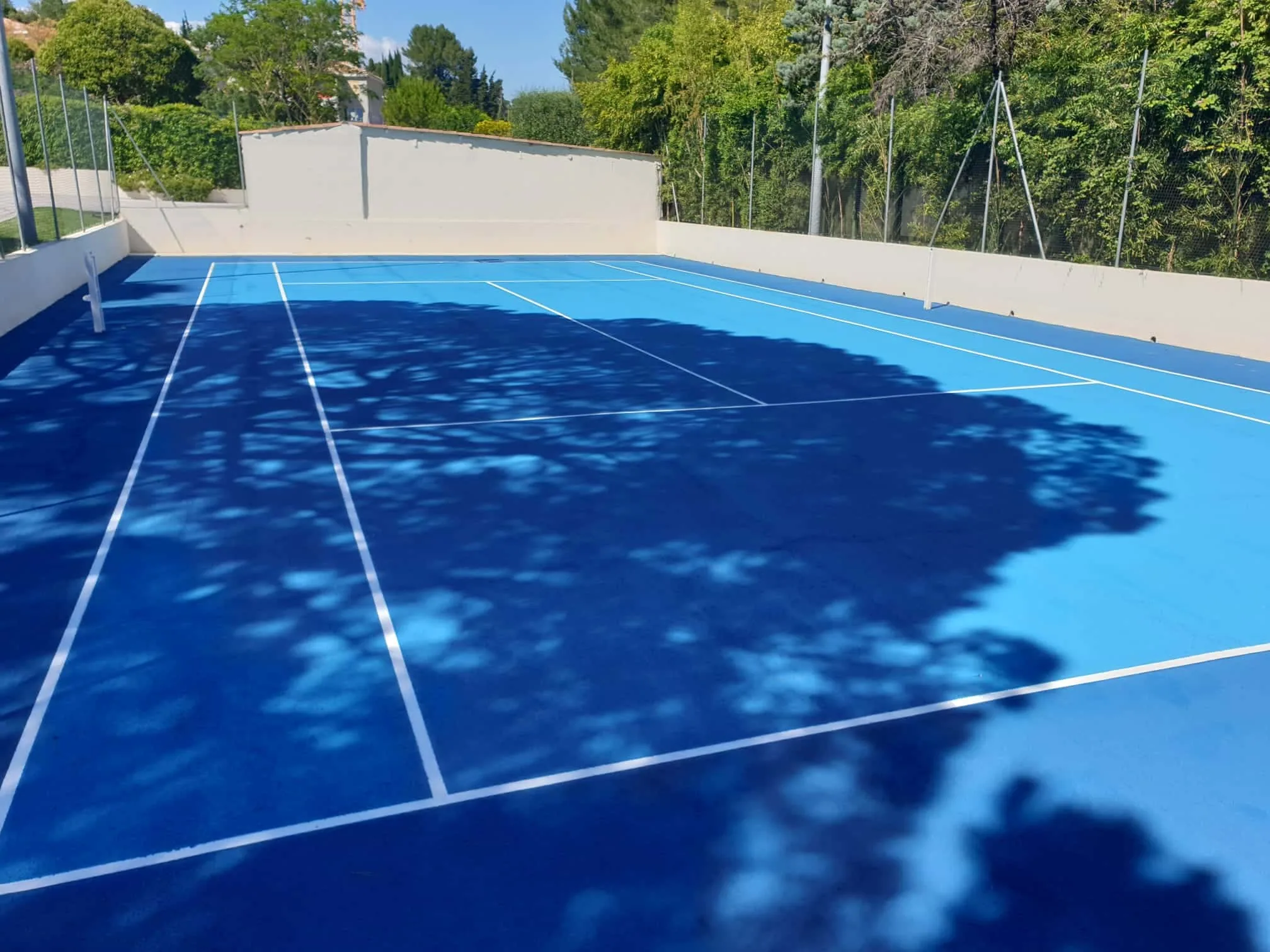 Court de tennis bleu ombragé au pied d'un mur