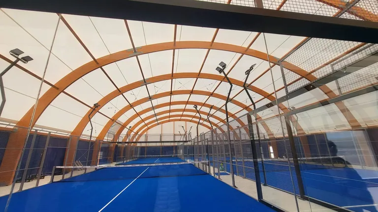 Court de tennis bleu sous une couverture à arches en bois