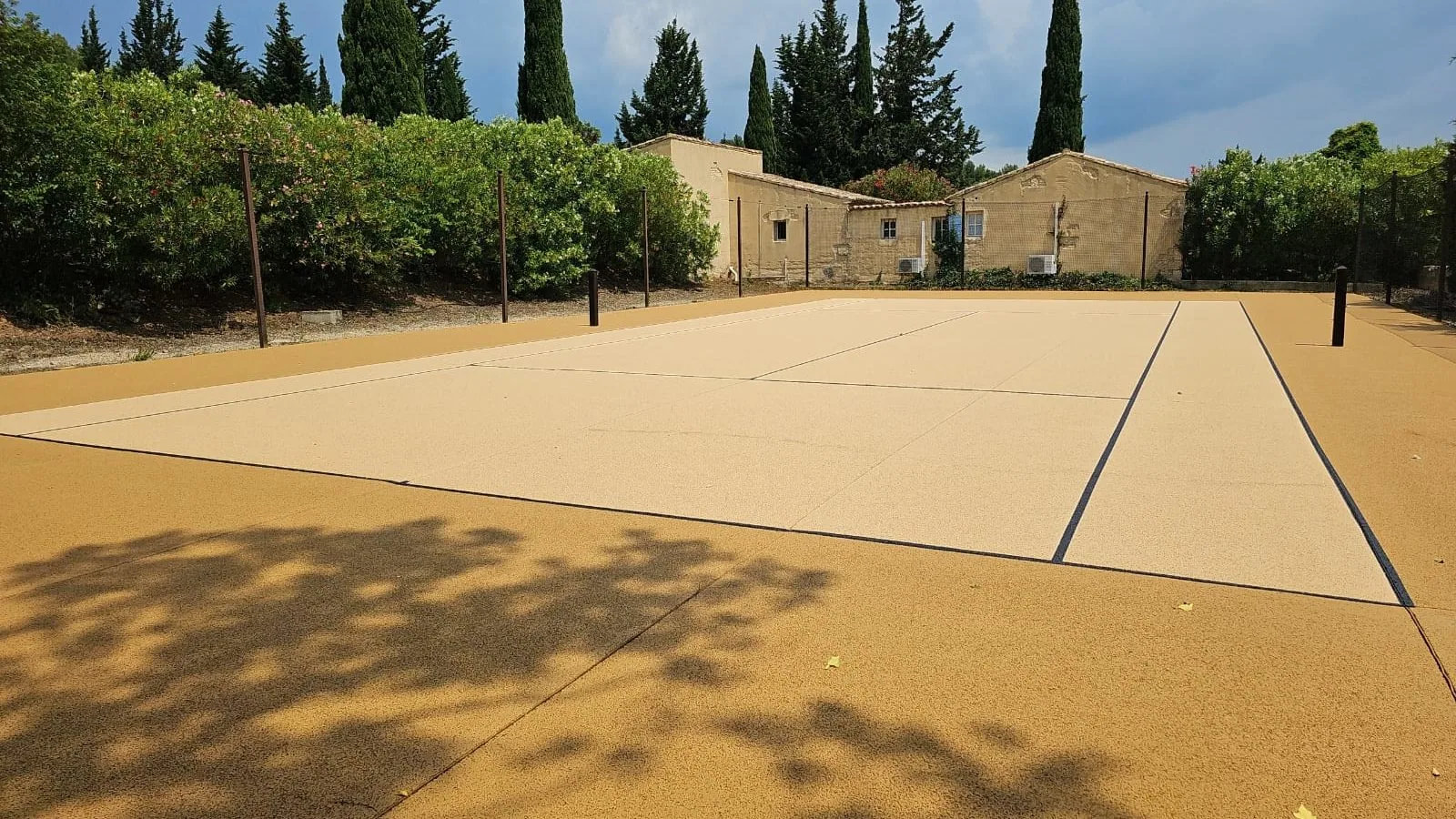Court de tennis couleur sable devant une bâtisse en pierre