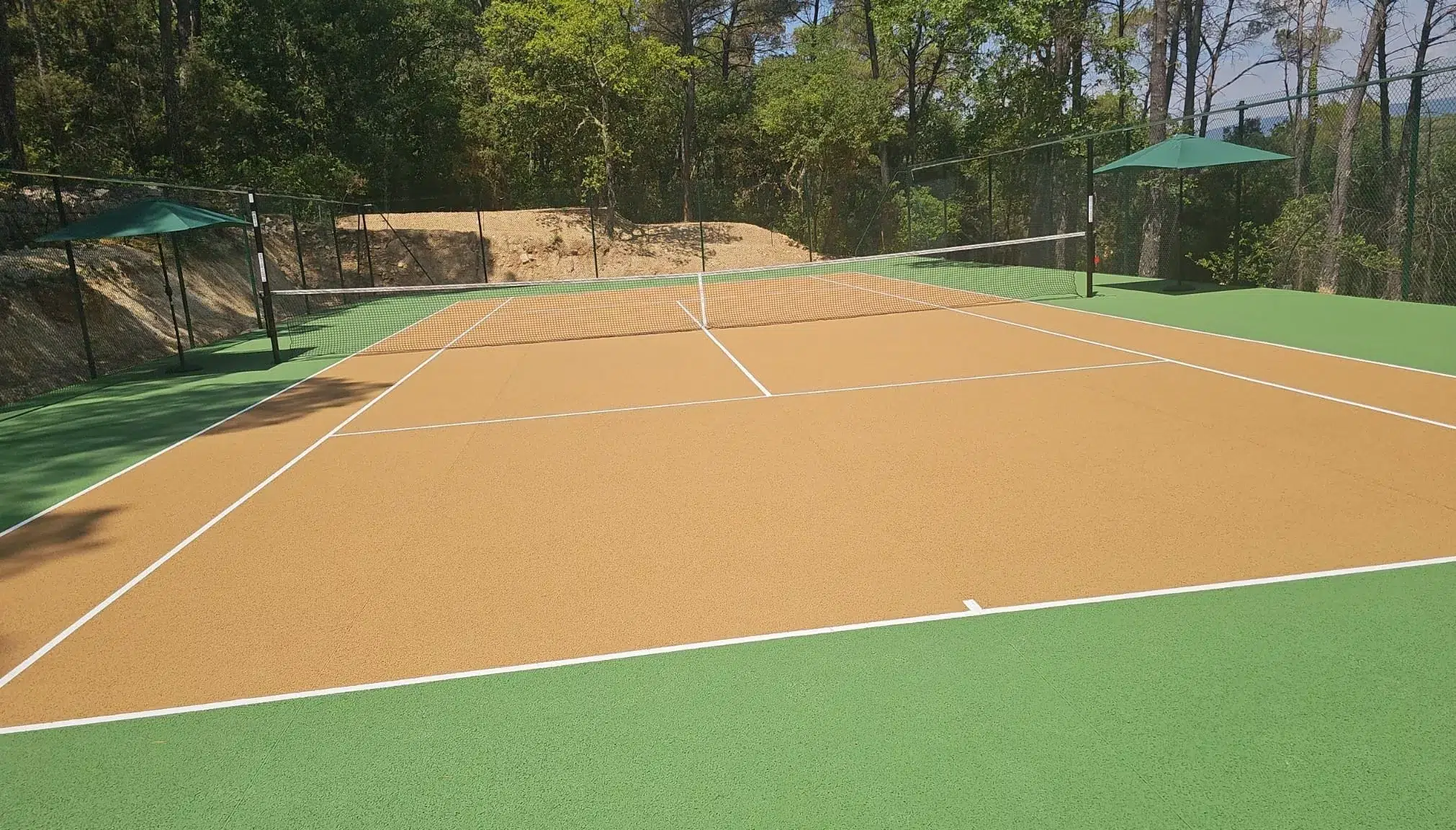 Court de tennis couleur terre battue et vert terminé dans une pinède