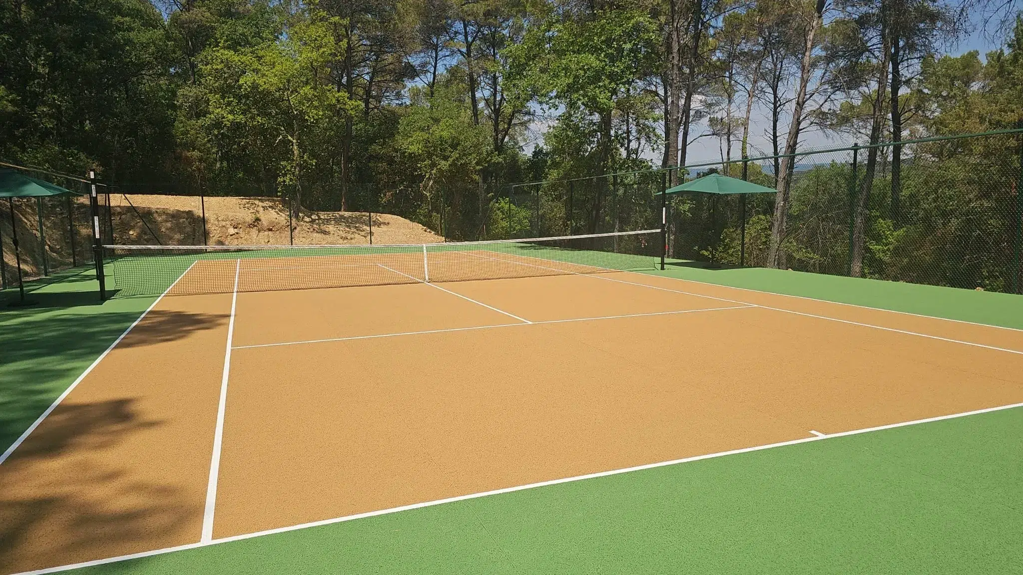 Court de tennis couleur terre battue neuf entouré de pins