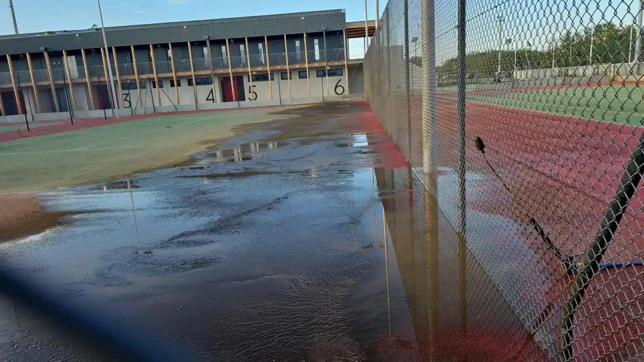 Court de tennis détrempé le long d'un bâtiment, avant reprise du drainage