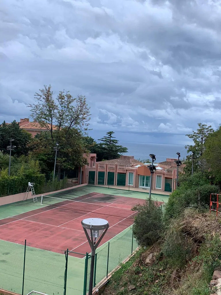 Court de tennis en contrebas d'une maison avec vue sur la mer