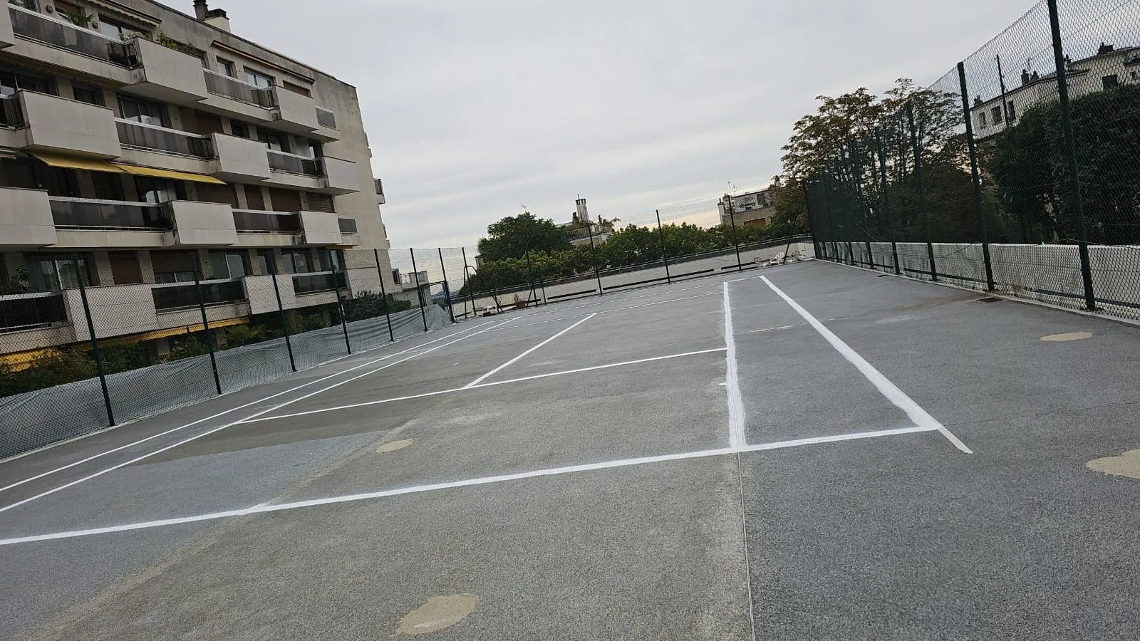 Court de tennis gris au pied d'un immeuble