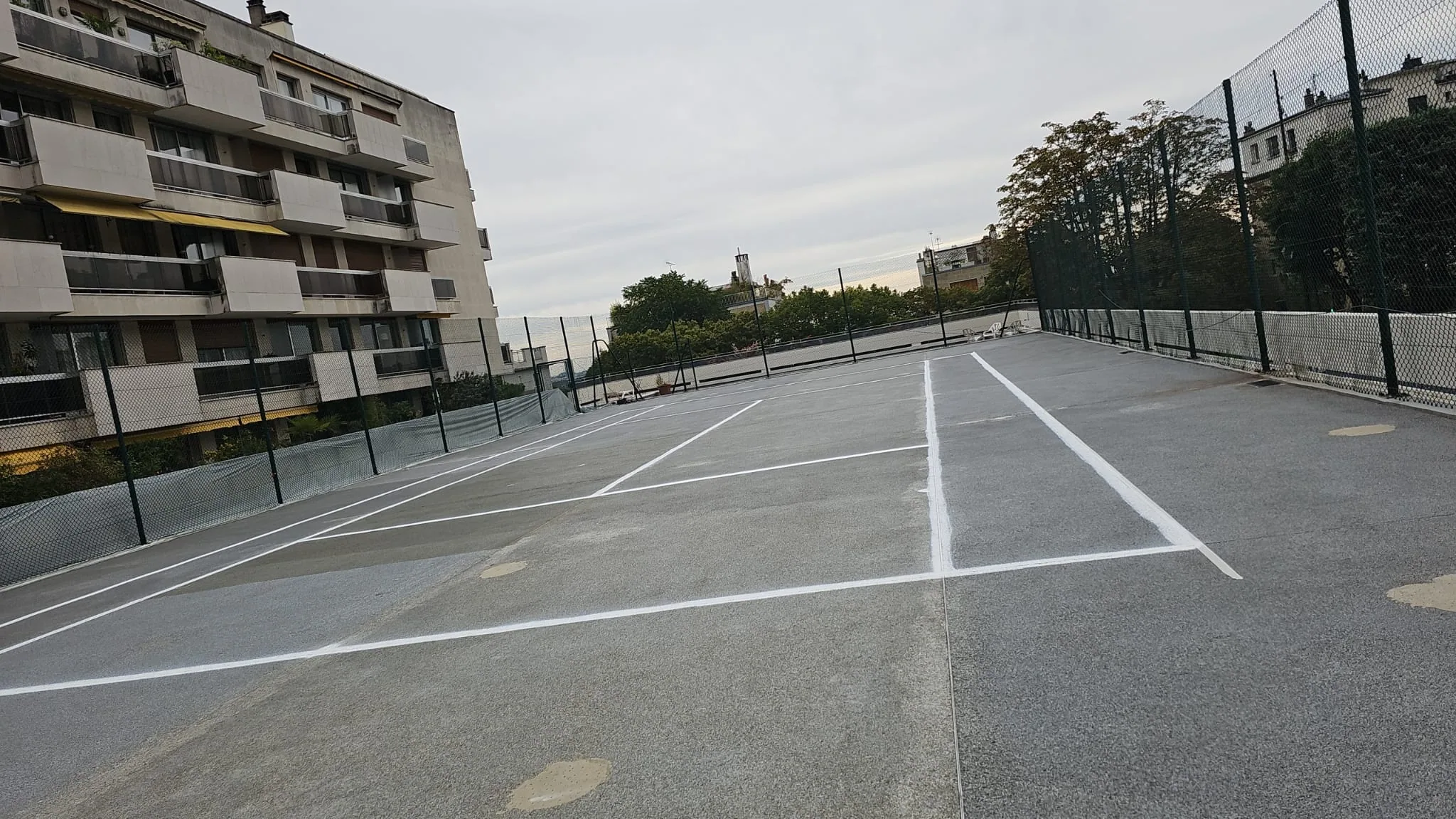 Court de tennis gris au pied d'un immeuble, lignes blanches