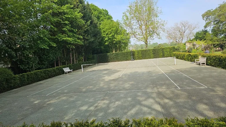 Court de tennis gris-vert à l'abandon, envahi par la végétation