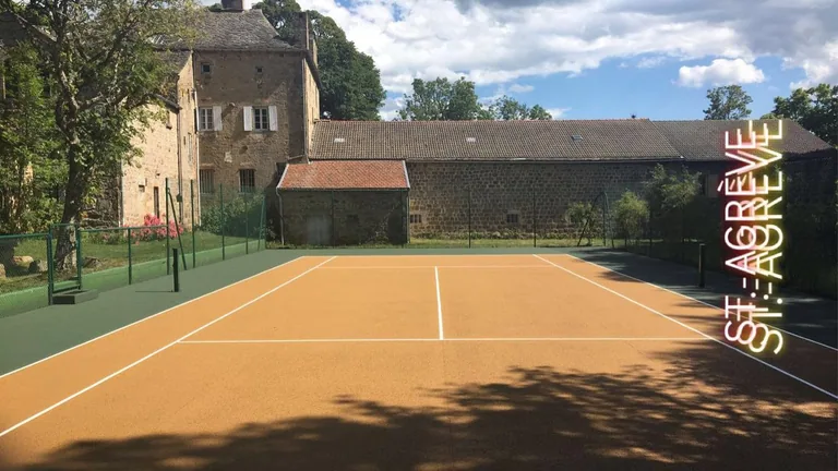 Court de tennis ocre devant une ancienne bâtisse en pierre