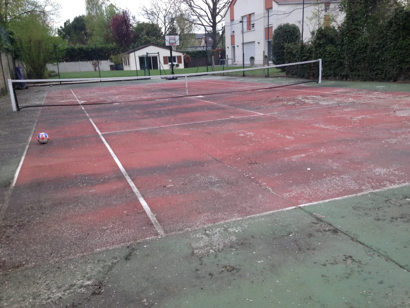 Court de tennis rouge abîmé et taché de mousse