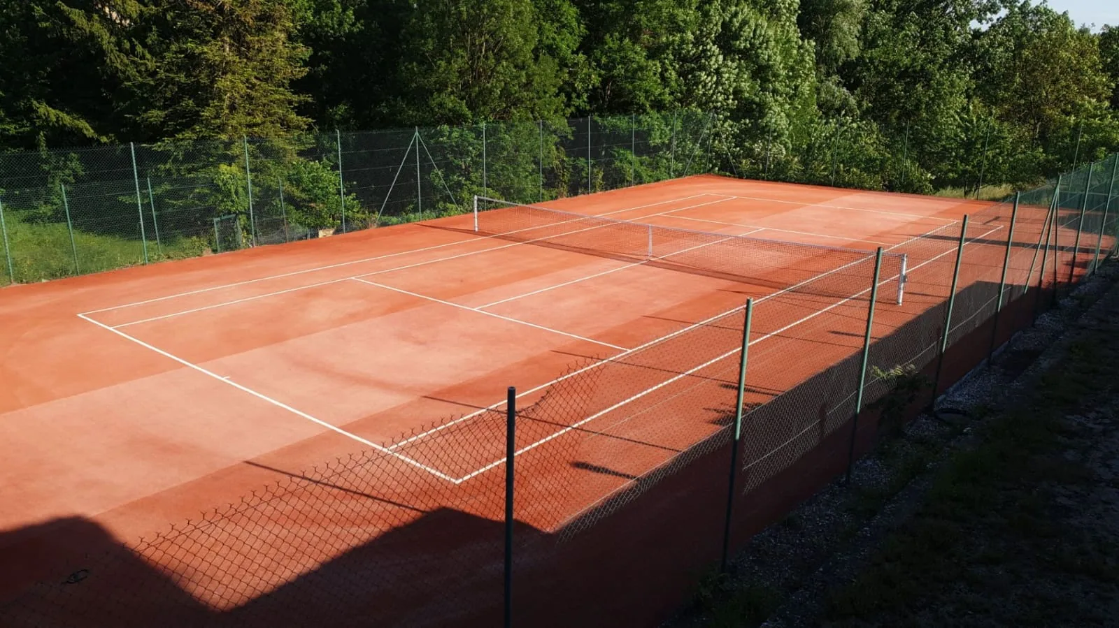 Court de tennis rouge clôturé dans un jardin