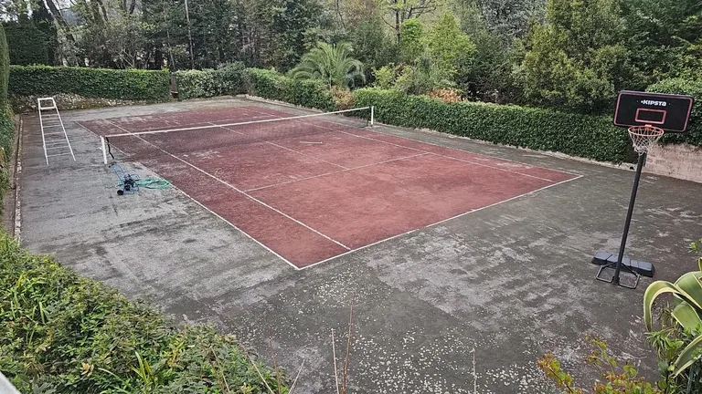 Court de tennis rouge encrassé avec panier de basket, avant rénovation