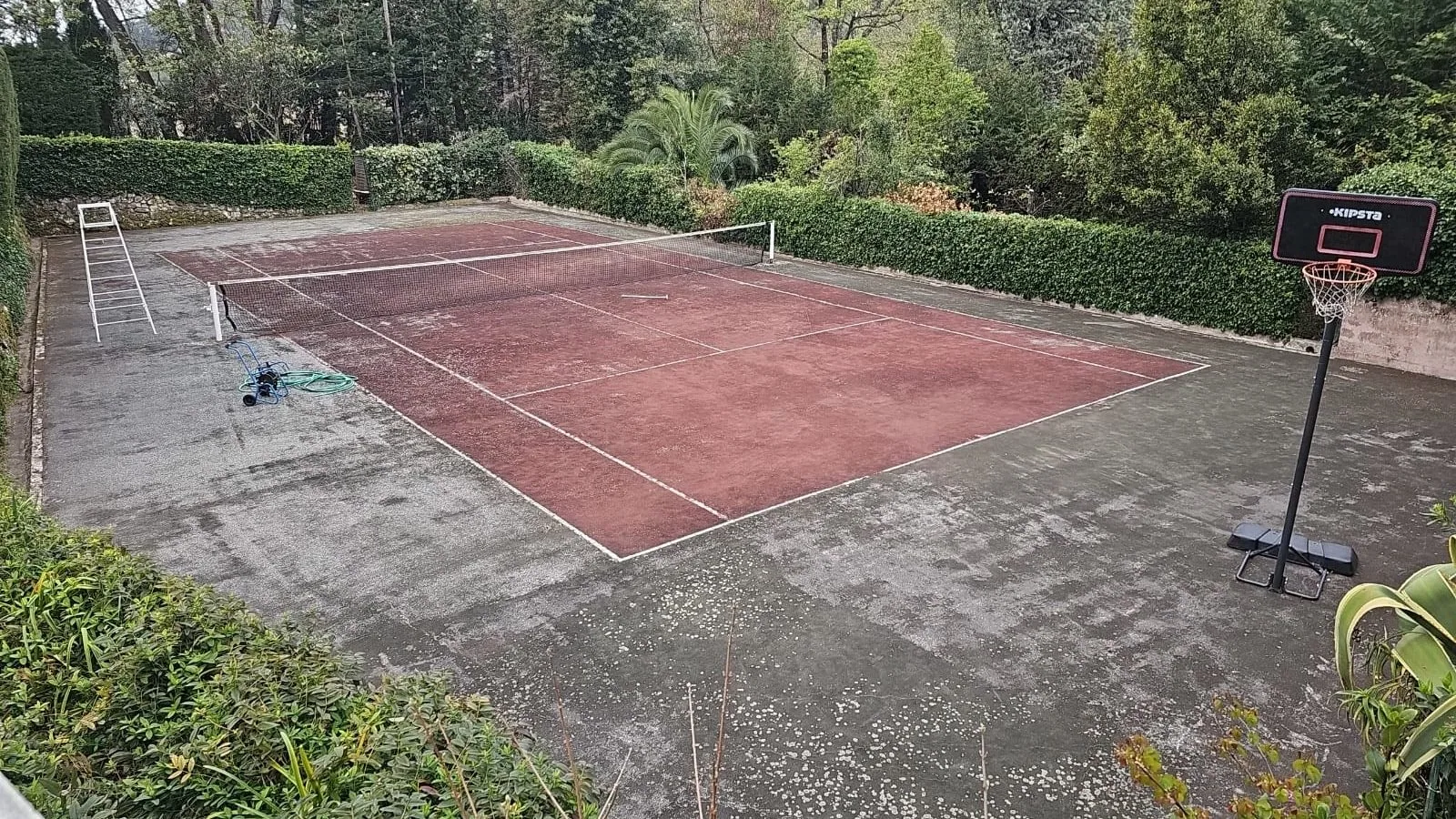 Court de tennis rouge encrassé avec panier de basket, avant rénovation
