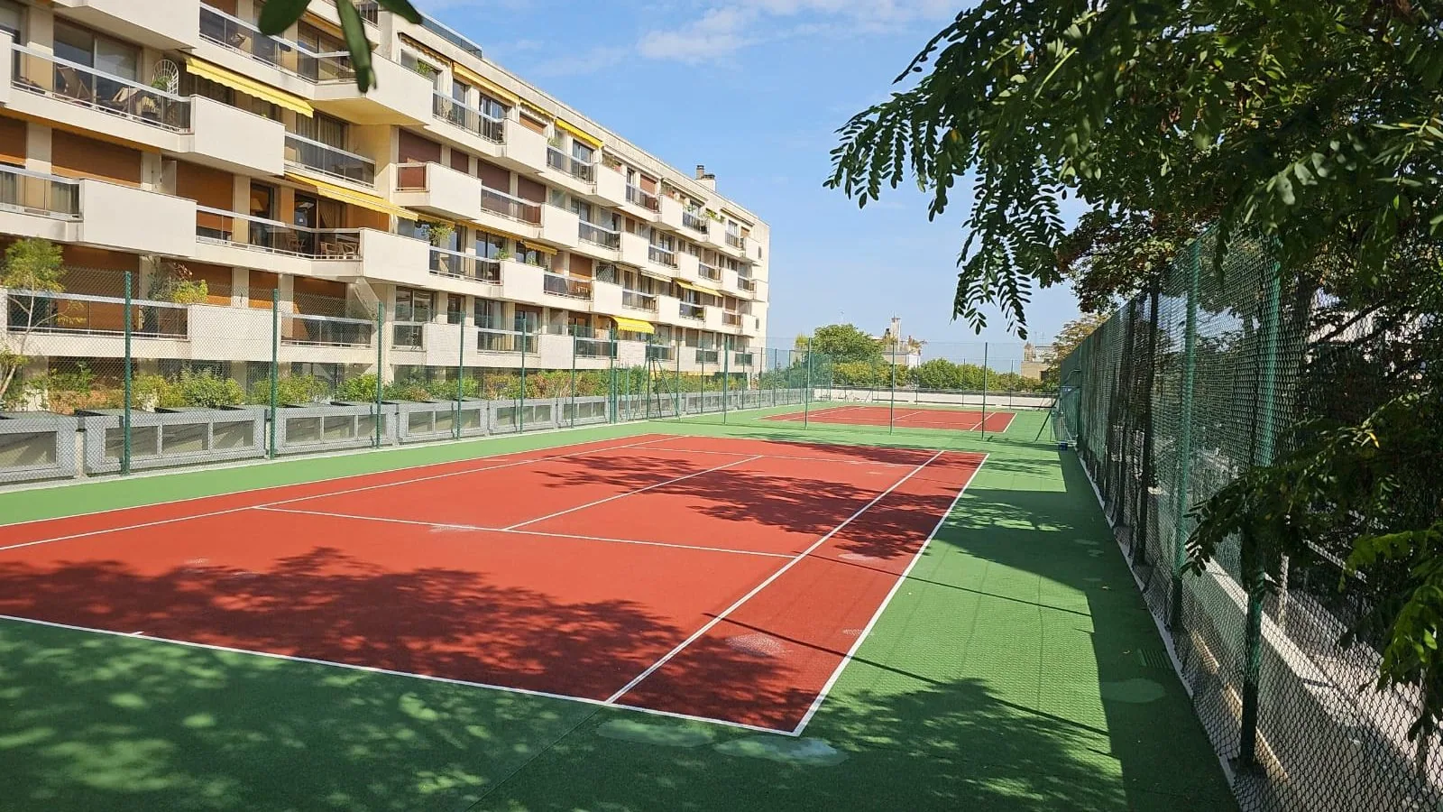 Court de tennis rouge et vert au pied d'un immeuble