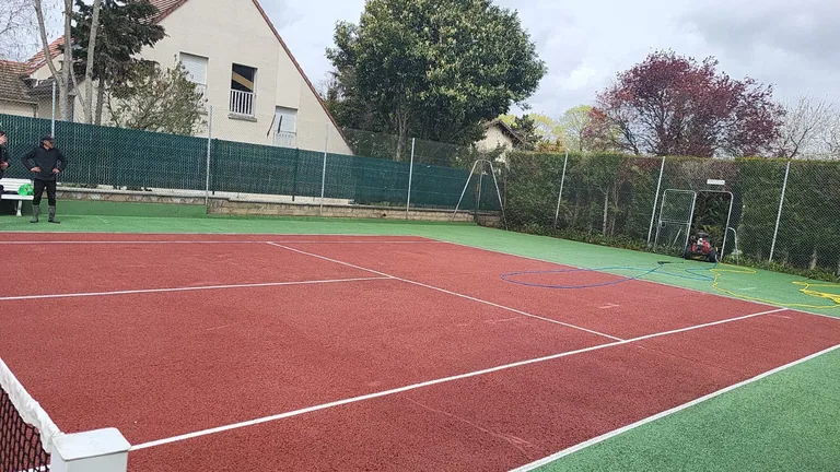 Court de tennis rouge et vert au pied d'une maison
