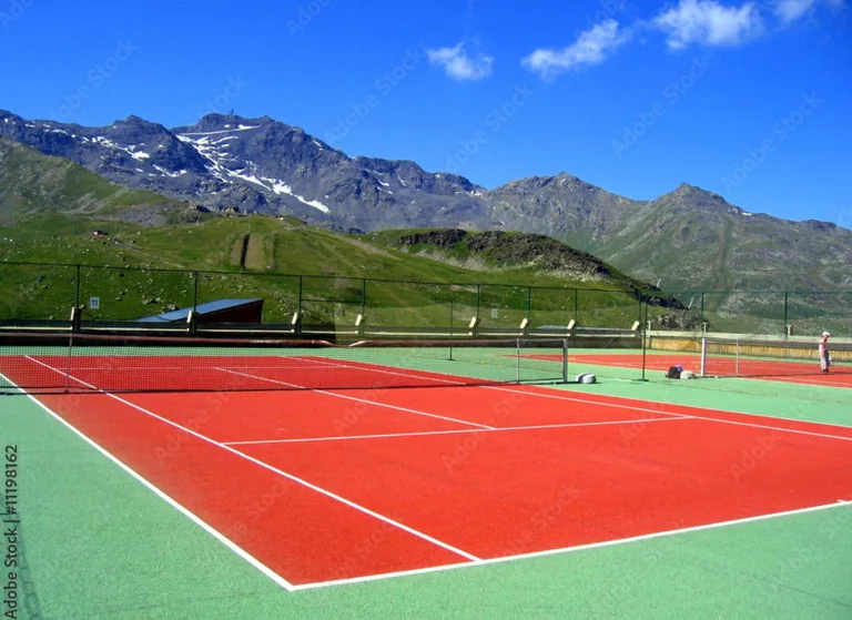 Court de tennis rouge et vert au pied des montagnes enneigées