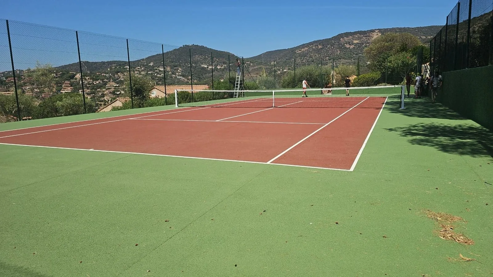 Court de tennis rouge et vert avec vue sur les collines