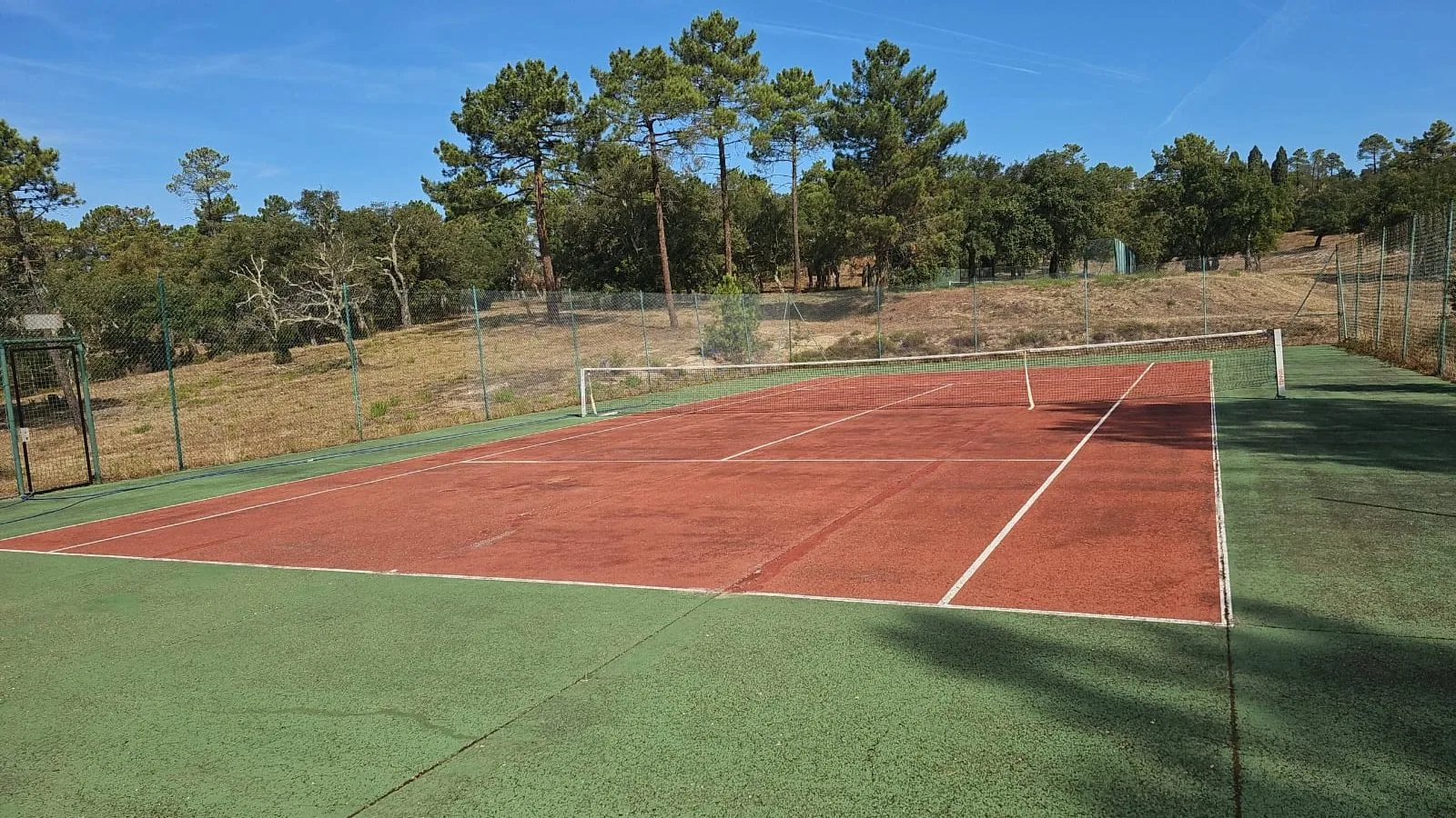 Court de tennis rouge et vert avec vue sur les pins