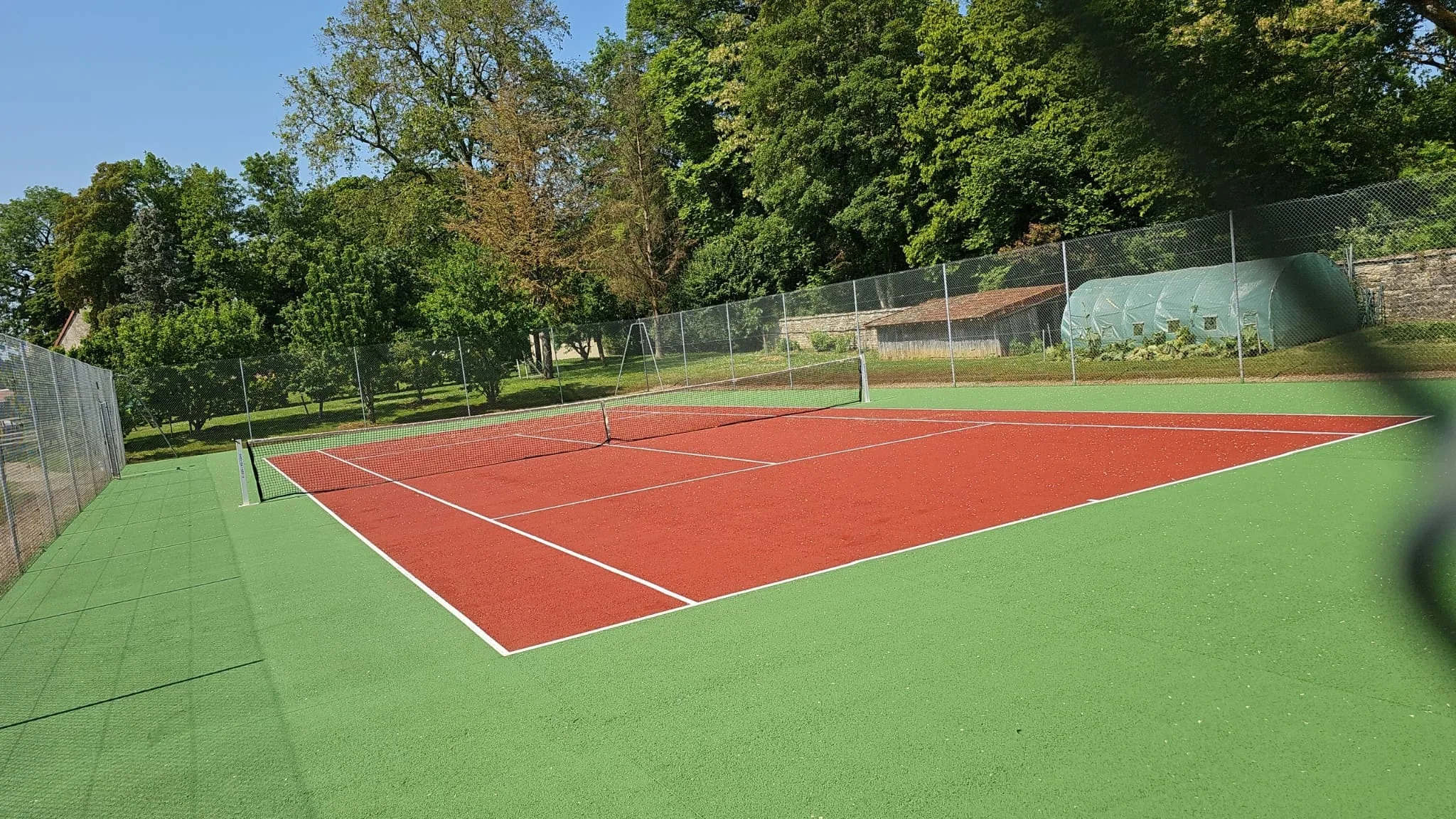 Court de tennis rouge et vert bordé d'arbres