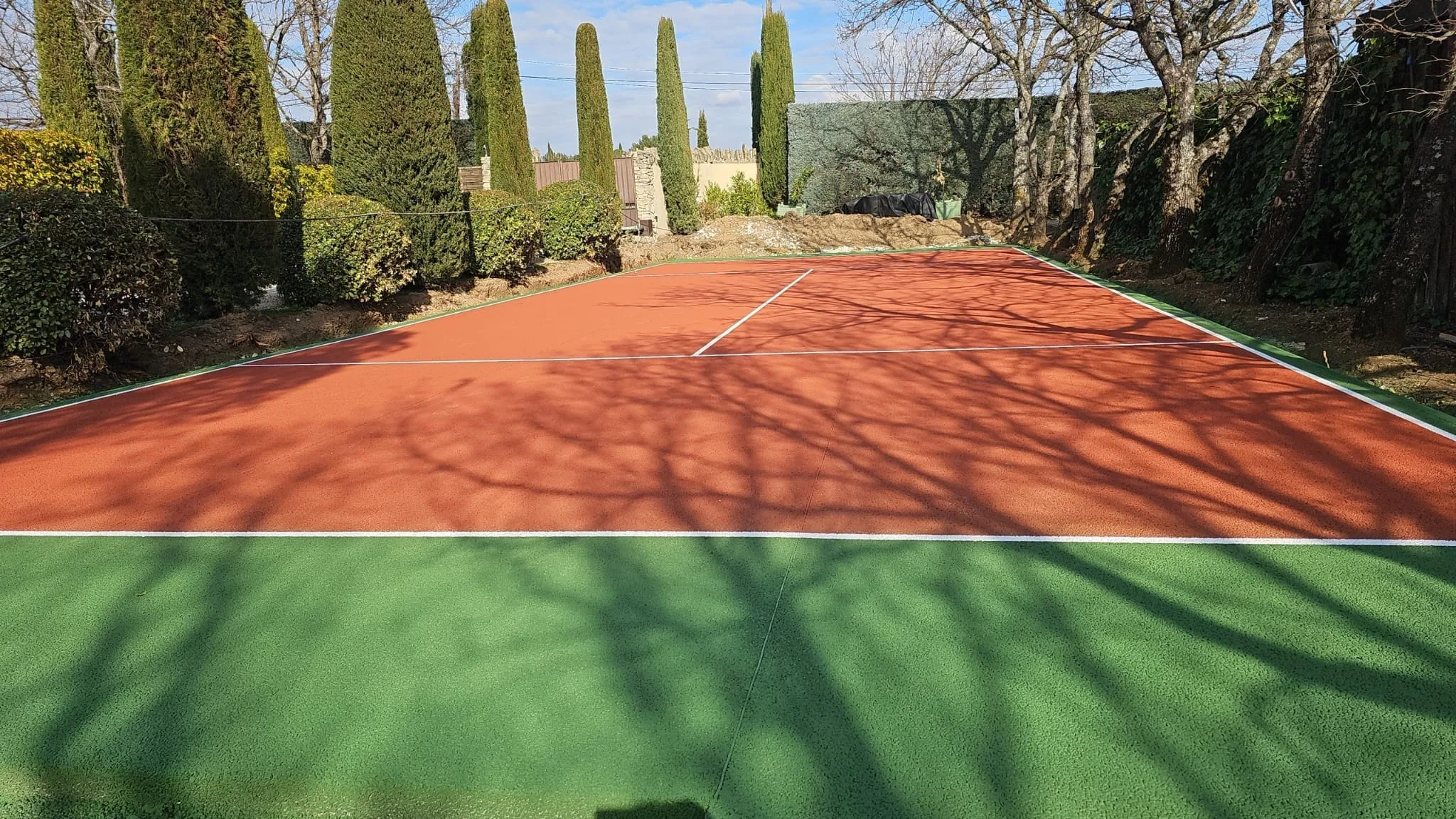 Court de tennis rouge et vert bordé de cyprès