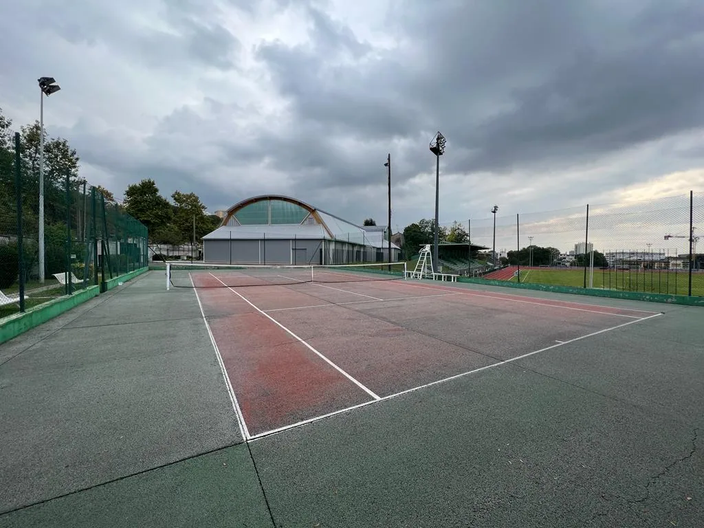 Court de tennis rouge et vert d'un club sous un ciel nuageux