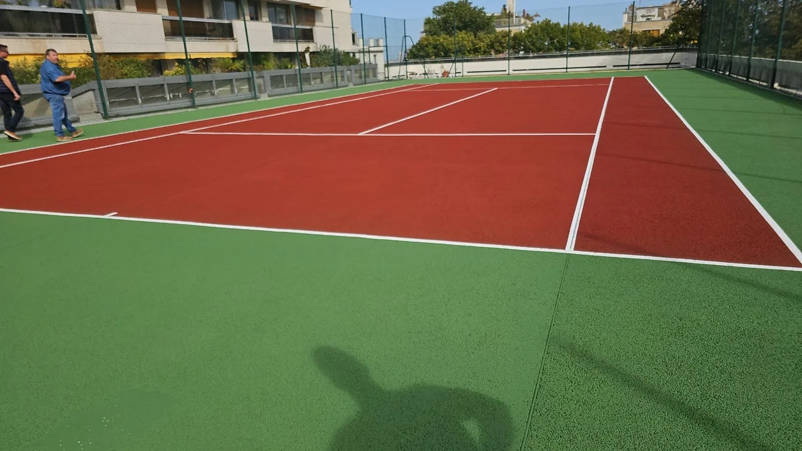 Court de tennis rouge et vert devant une résidence