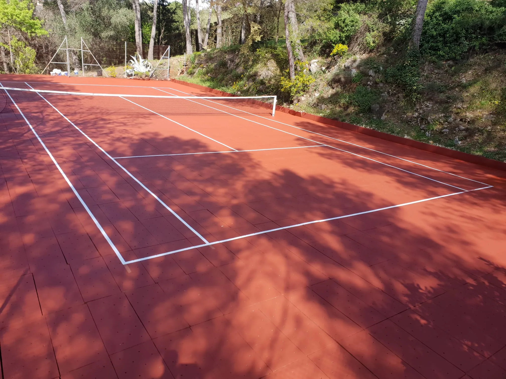 Court de tennis rouge ombragé par les arbres
