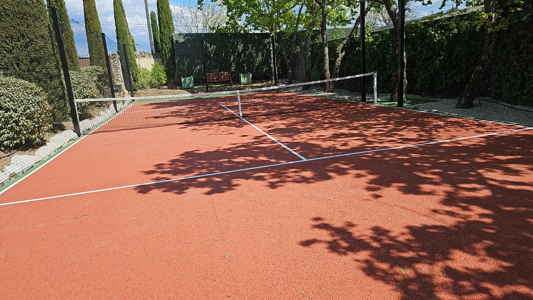 Court de tennis rouge ombragé par les arbres