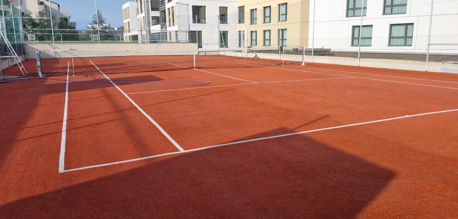 Court de tennis rouge-orangé devant un immeuble récent