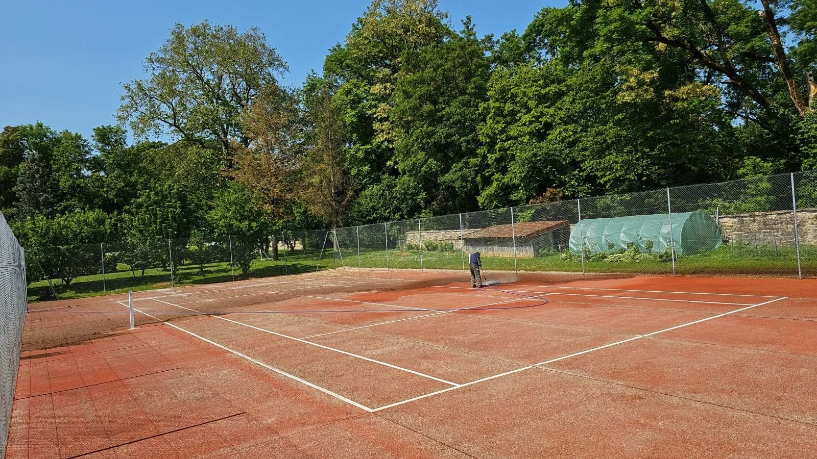 Court de tennis rouge pendant la rénovation, ouvrier sur le court