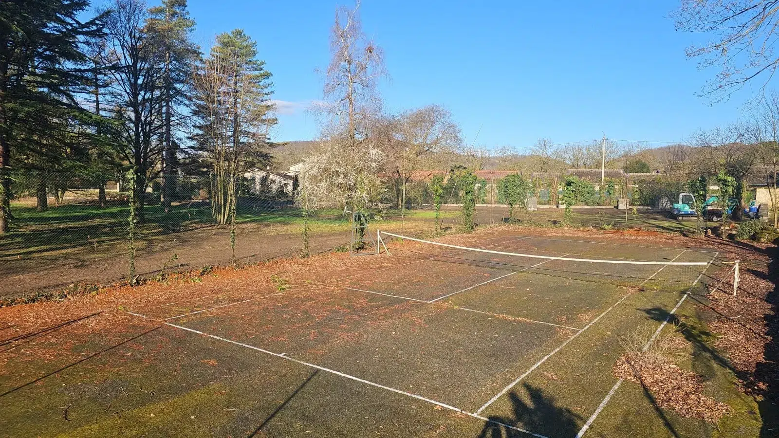 Court de tennis rouge terni dans un jardin, avant rénovation