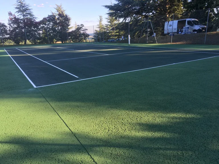 Court de tennis vert à l'ombre de grands arbres