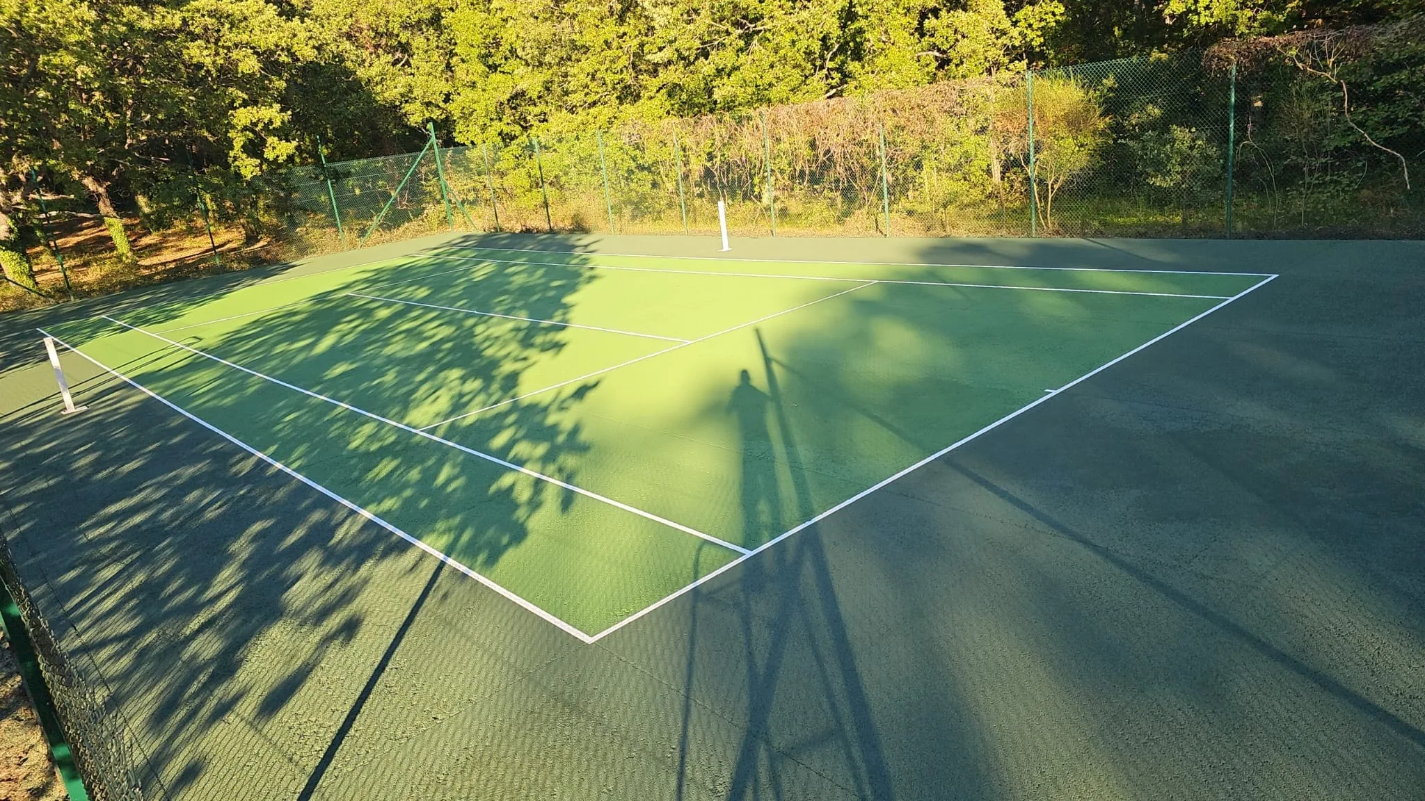Court de tennis vert à l'ombre de la clôture