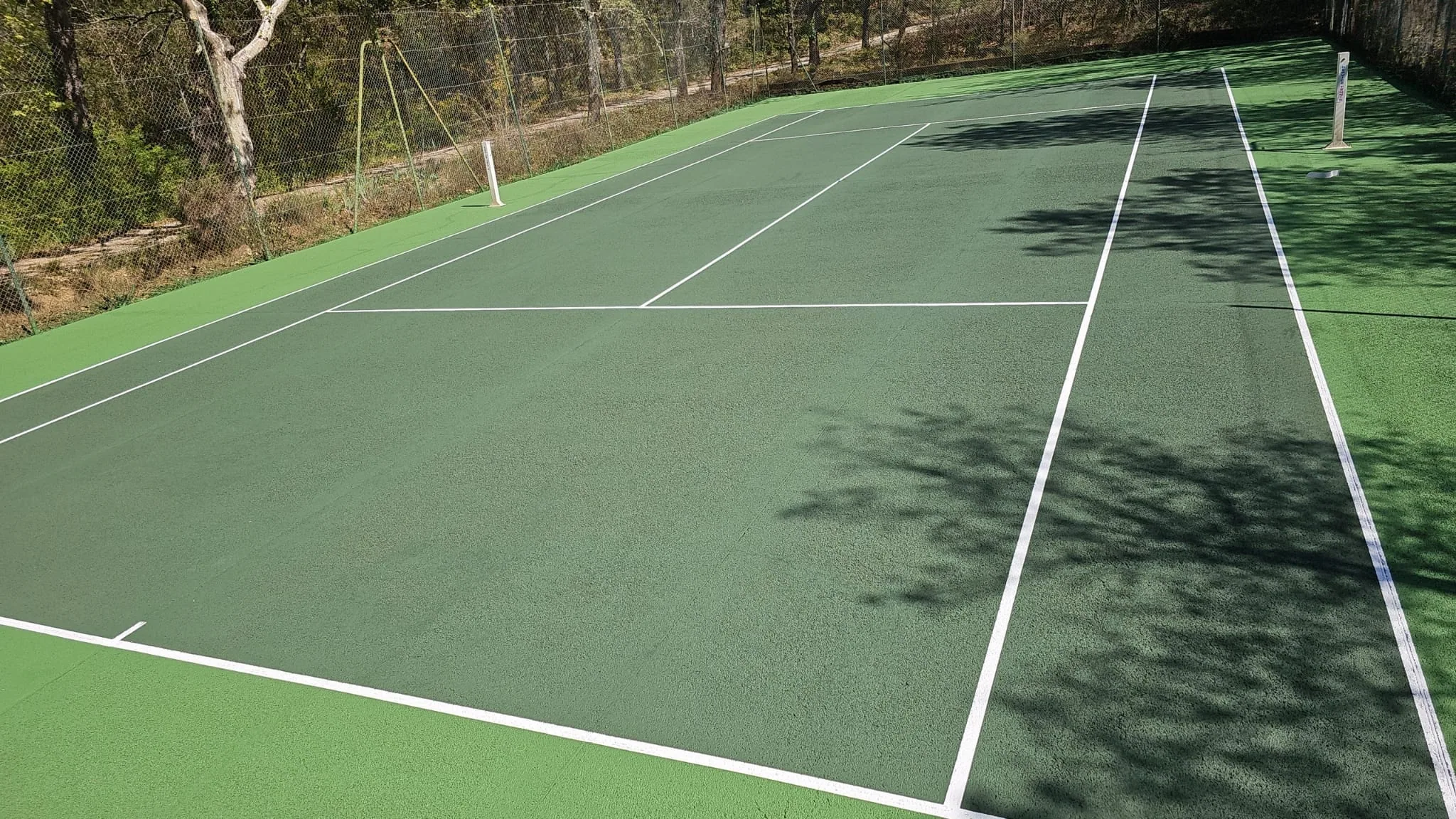 Court de tennis vert à l'ombre portée des arbres