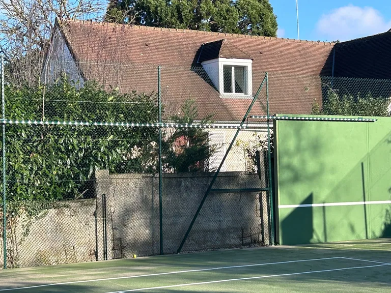 Court de tennis vert clôturé au pied d'une maison