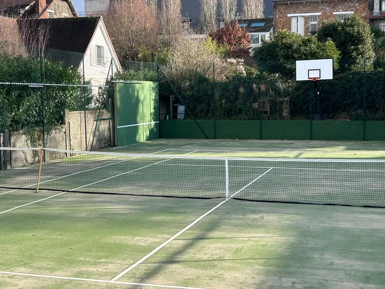Court de tennis vert encrassé au pied d'une maison