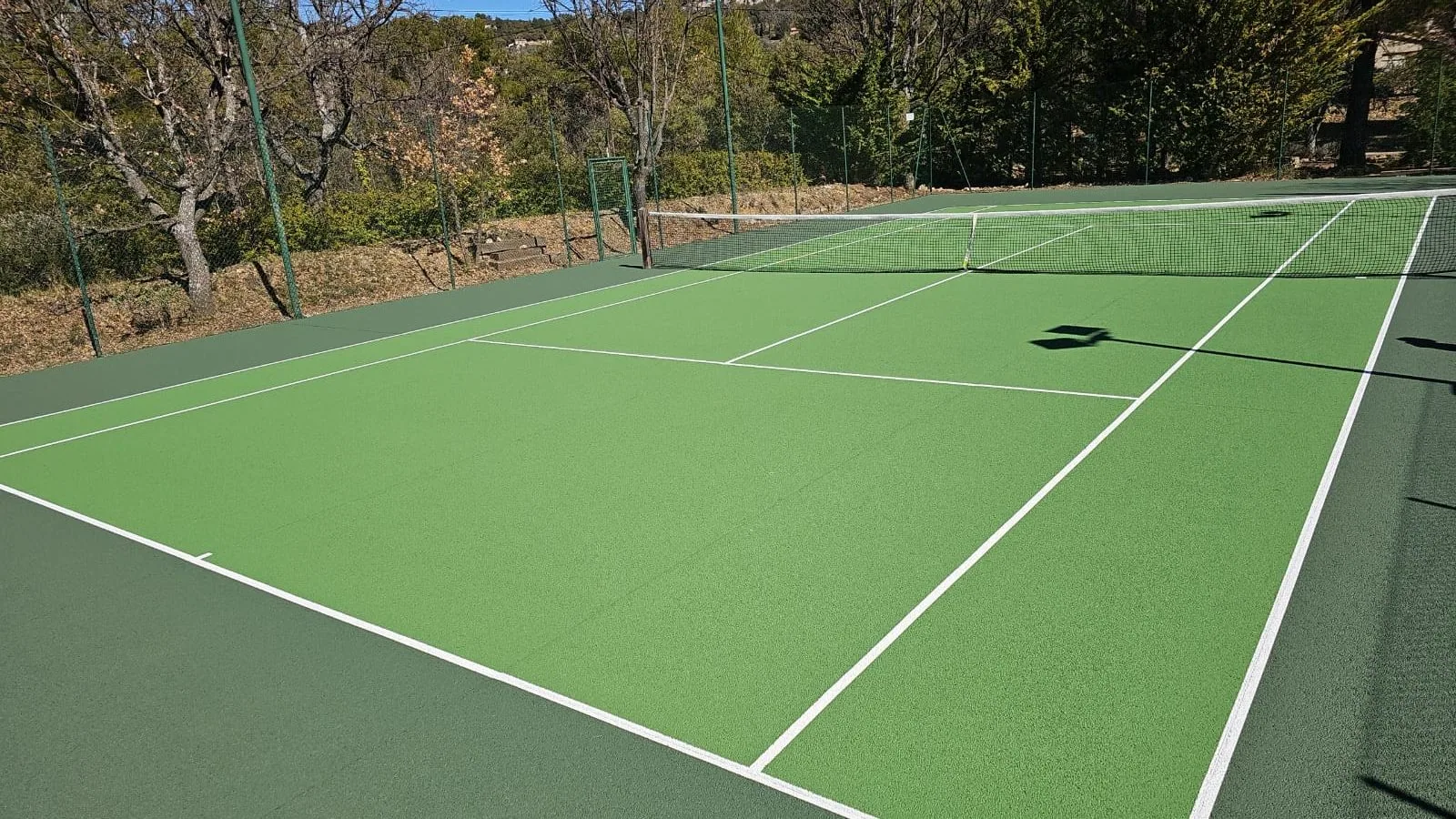 Court de tennis vert et vert foncé en contrebas d'un verger