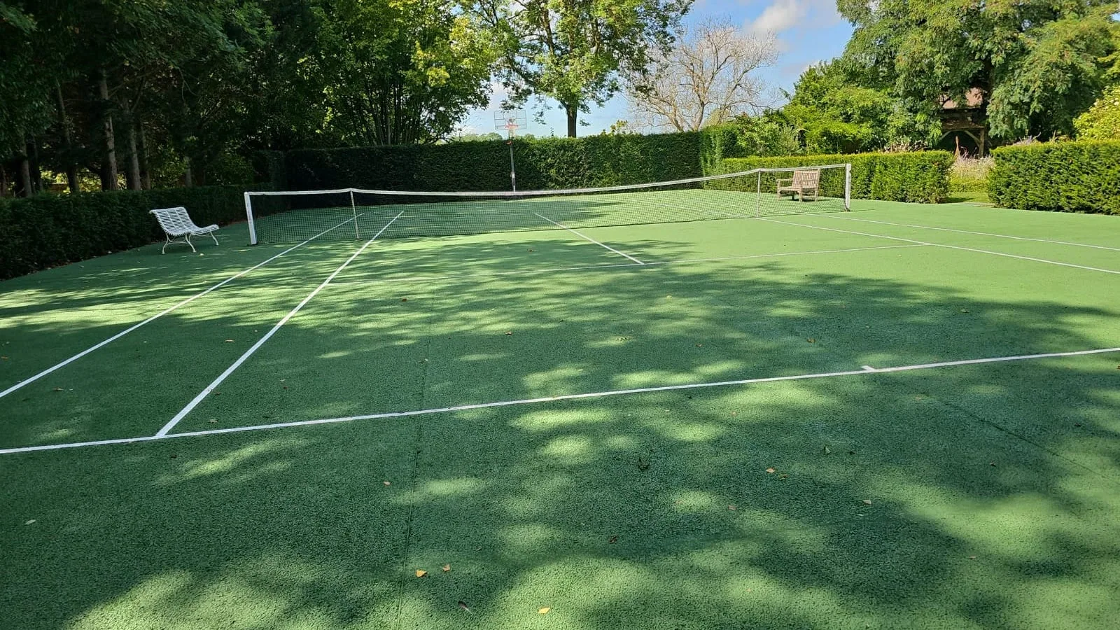 Court de tennis vert ombragé après nettoyage