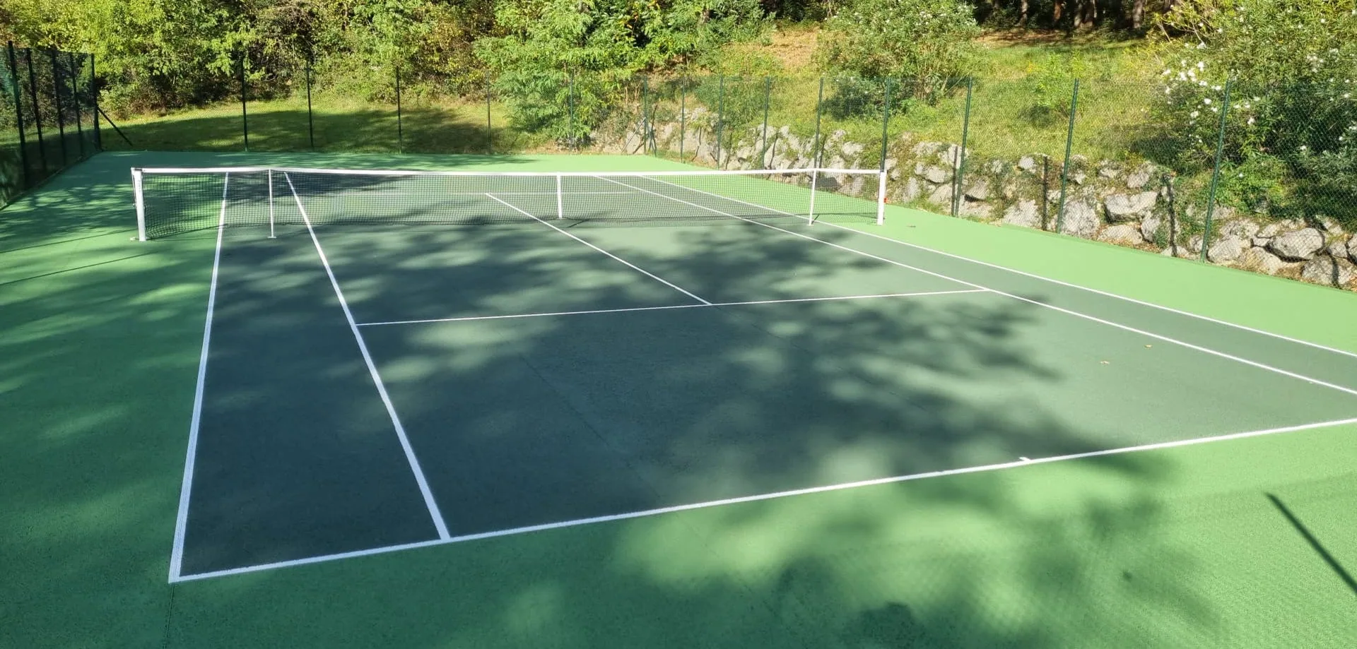 Court de tennis vert ombragé par les arbres