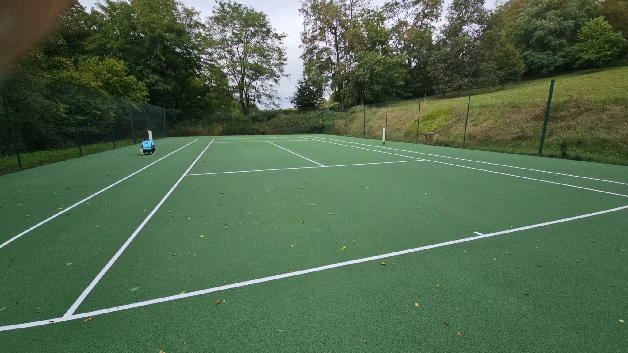 Court de tennis vert rénové entouré de végétation