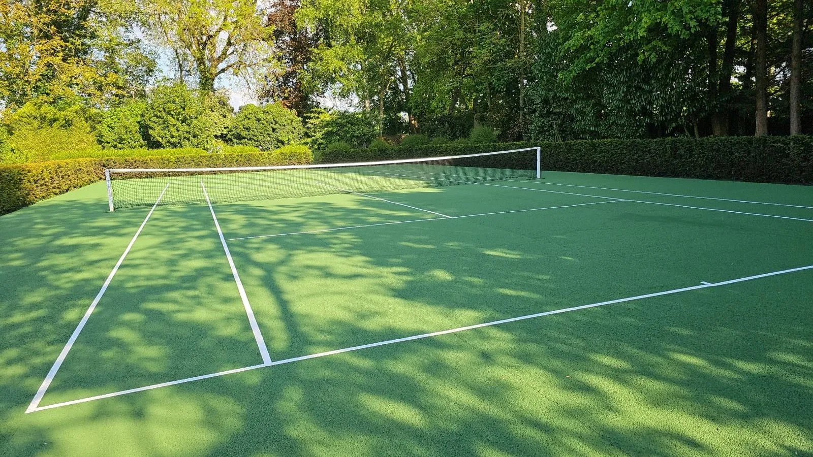 Court de tennis vert sous les arbres, lignes blanches neuves