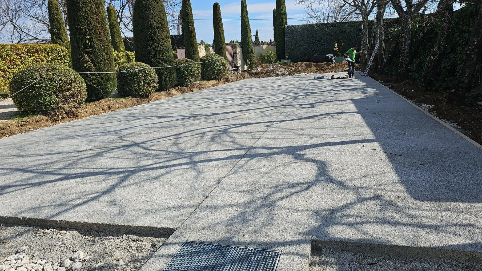 Dalle de béton d'un futur court bordée de cyprès