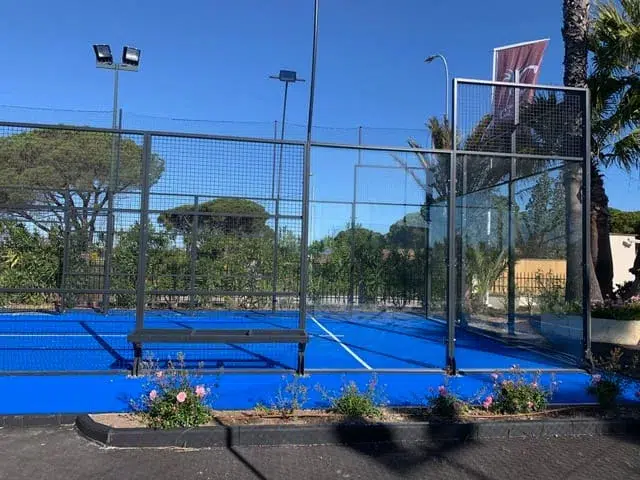 Terrain de padel bleu entouré de vitrages et d'éclairages