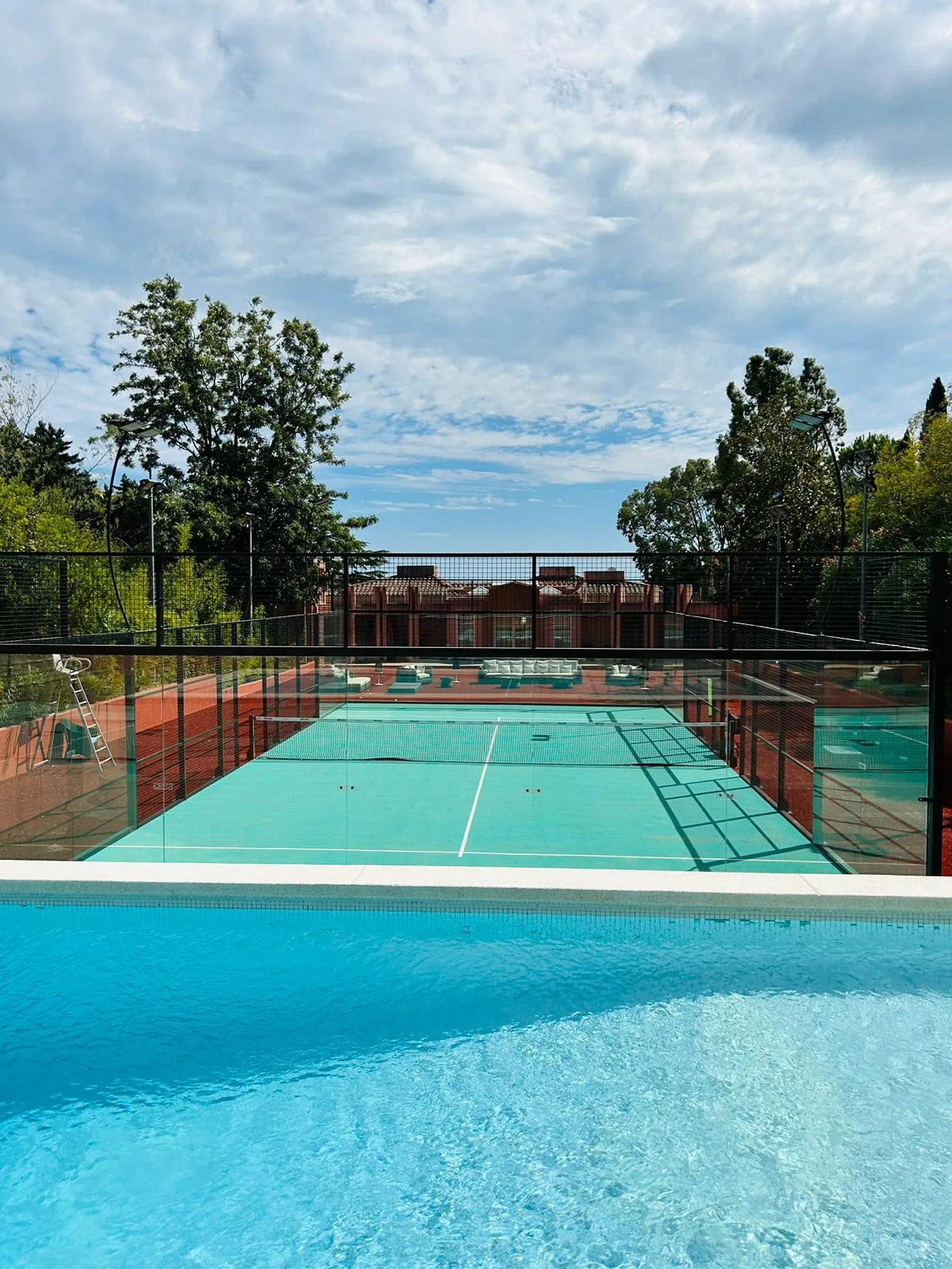 Terrain de padel turquoise au bord d'une piscine avec vue sur la mer