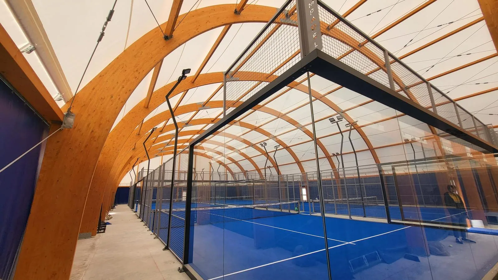 Terrains de padel bleus sous une charpente à arches en bois